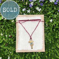 adjustable necklace: yellow bronze charm wrapped with indigo-dyed silk thread on burgundy crocheted cord