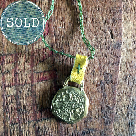 necklace: yellow bronze charm with green cord